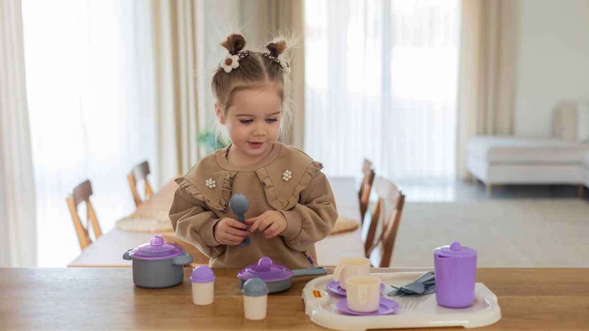 Little girl enjoying imaginative play with toy kitchen set in a cozy, well-lit room.